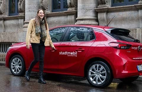 Eine Frau greift nach dem Türgriff eines am Straßenrand geparkten roten stadtmobil Fahrzeugs.
